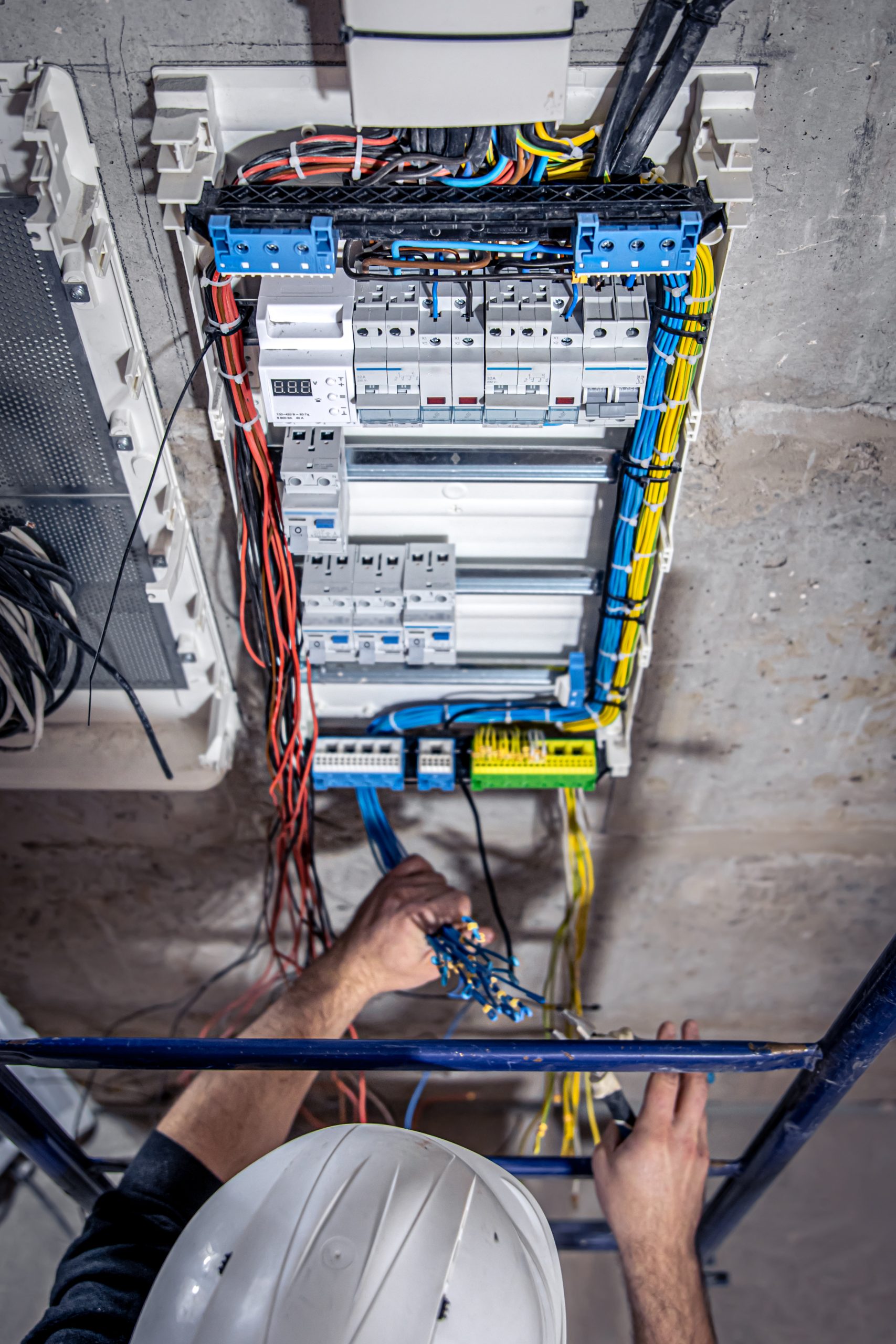 A male electrician works in a switchboard with an electrical connecting cable, connects the equipment with tools, top view.